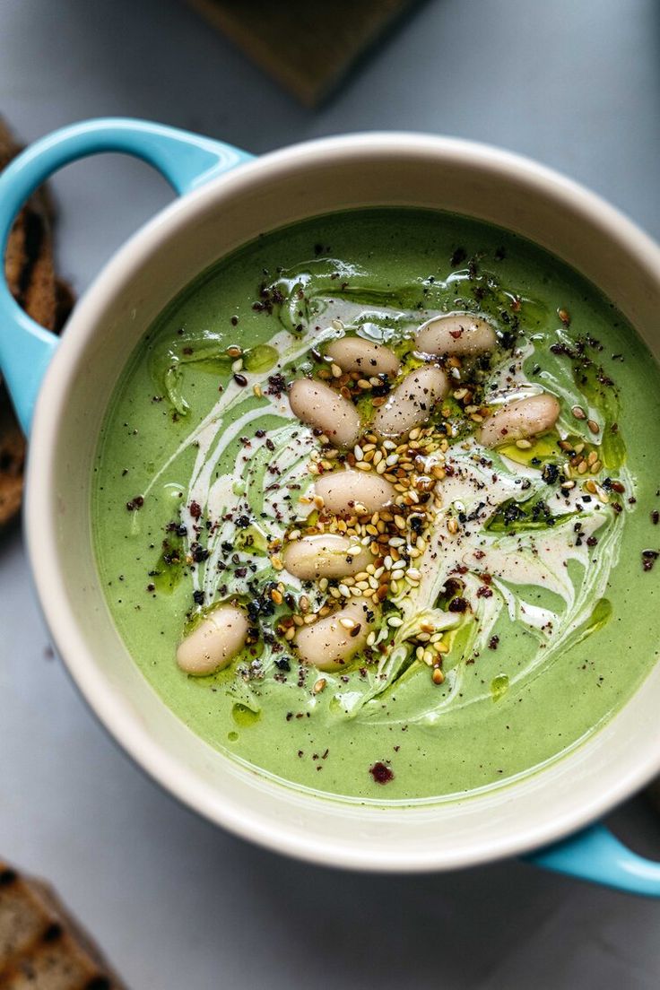 a white bowl filled with green soup on top of a blue table next to crackers