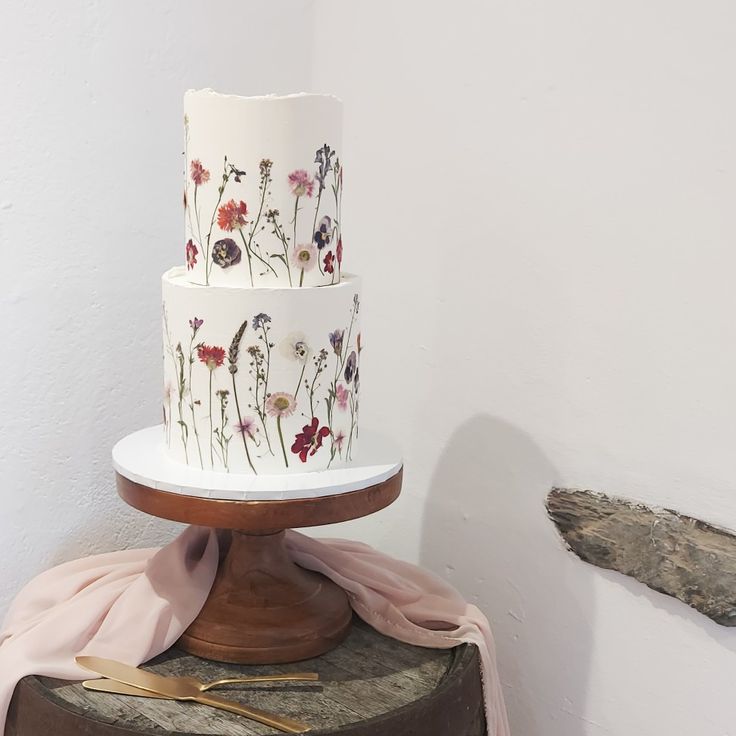 a three tiered cake with flowers painted on the side and gold serving utensils