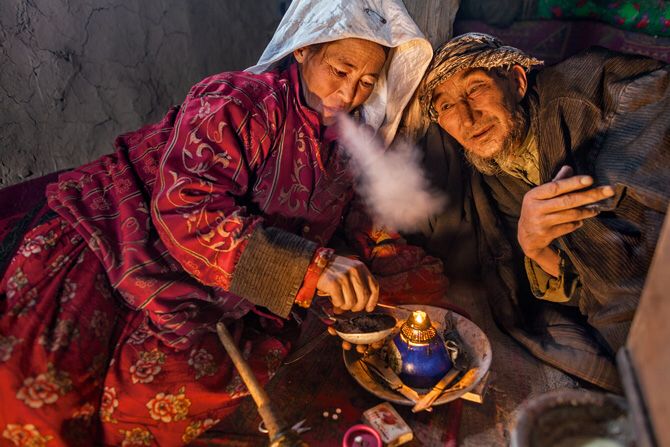 an old man and woman sitting next to each other in front of a tea pot