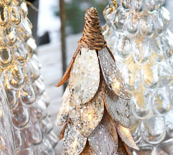 three glass christmas trees with lights on them in front of snow covered branches and other decorations