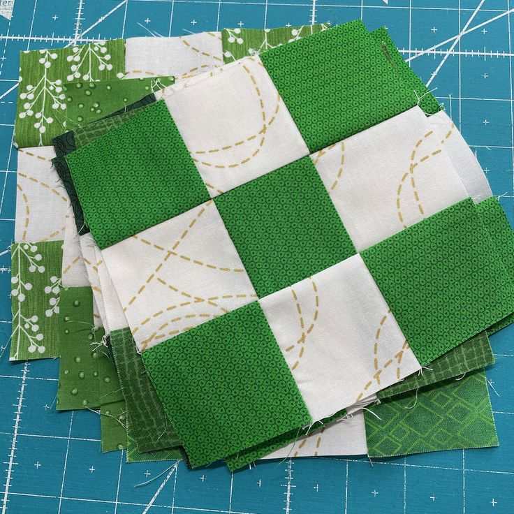 four green and white patchwork squares on a cutting board next to a ruler with one piece cut out