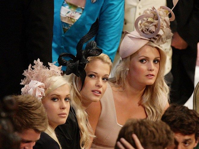 two women sitting next to each other at a formal event with hats on their heads