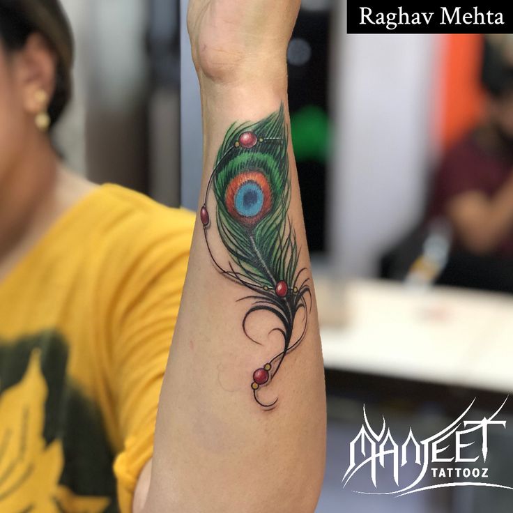 a woman's arm with a peacock feather tattoo on her left wrist and the words rachav meha above it