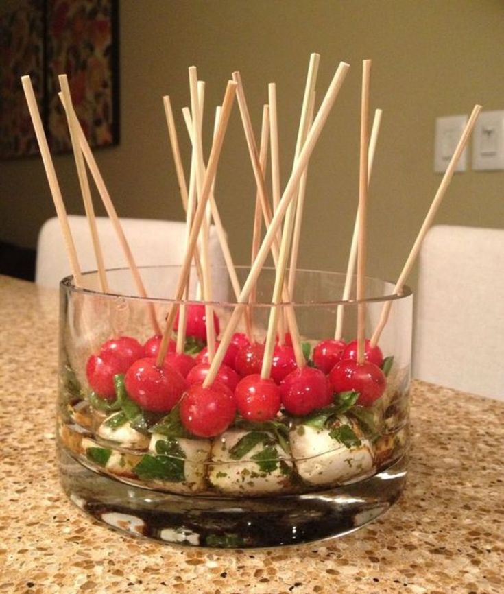 a glass bowl filled with tomatoes and skewers on top of a marble counter