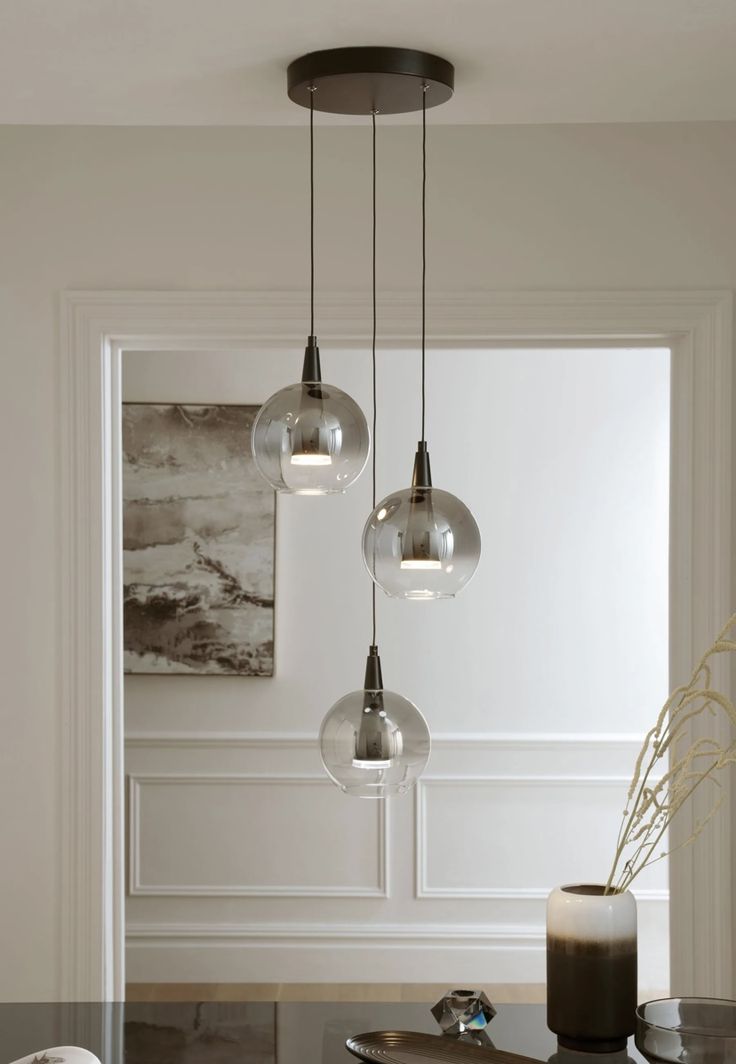 three glass globes hang from the ceiling above a dining room table with two vases on it