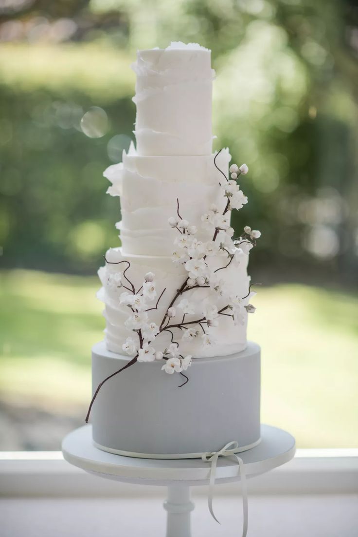 a wedding cake with white flowers on top is sitting on a table in front of a window