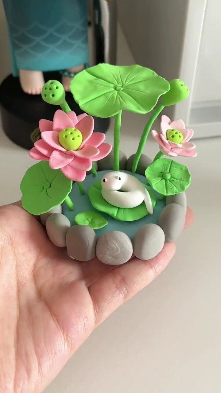 a hand is holding a small toy pond with flowers