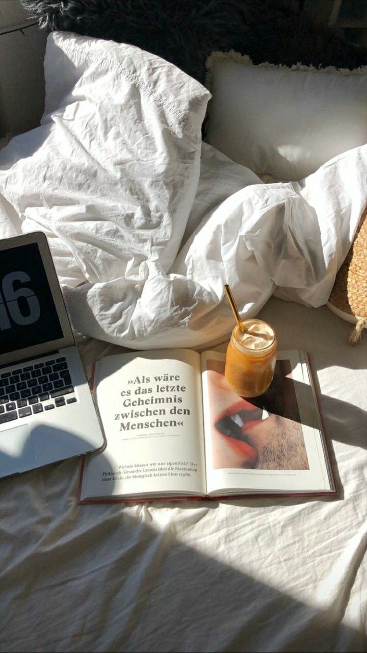 an open laptop computer sitting on top of a bed next to a book and drink