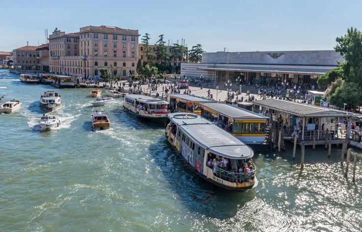 several boats are traveling down the river in front of some buildings and people walking around