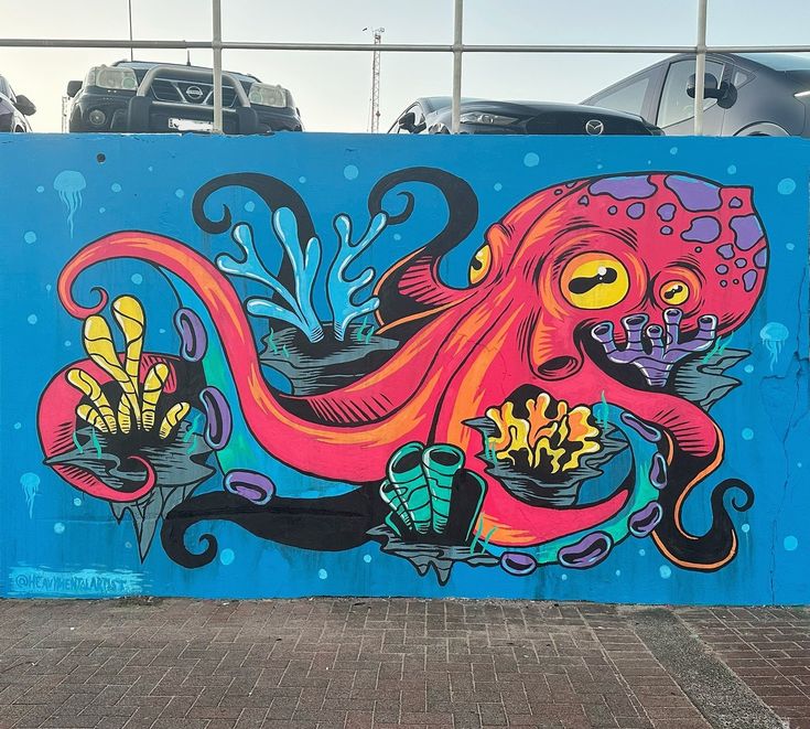 an octopus mural painted on the side of a blue wall in front of parked cars