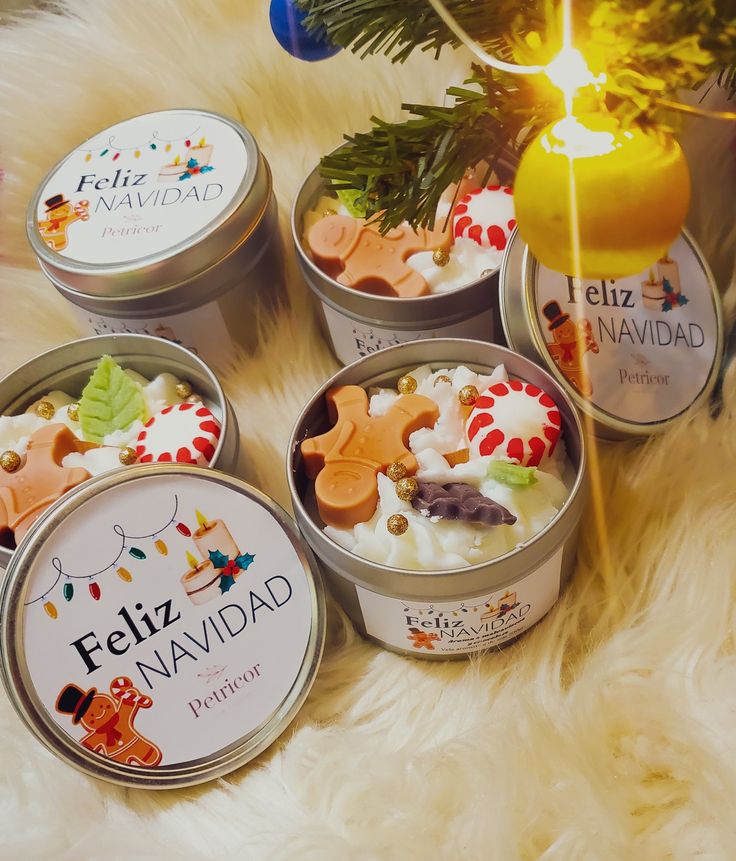 four tins of candles sitting on top of a white fur covered floor next to a christmas tree