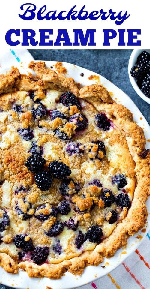 blackberry cream pie on a white plate with blueberries and blackberries in the background