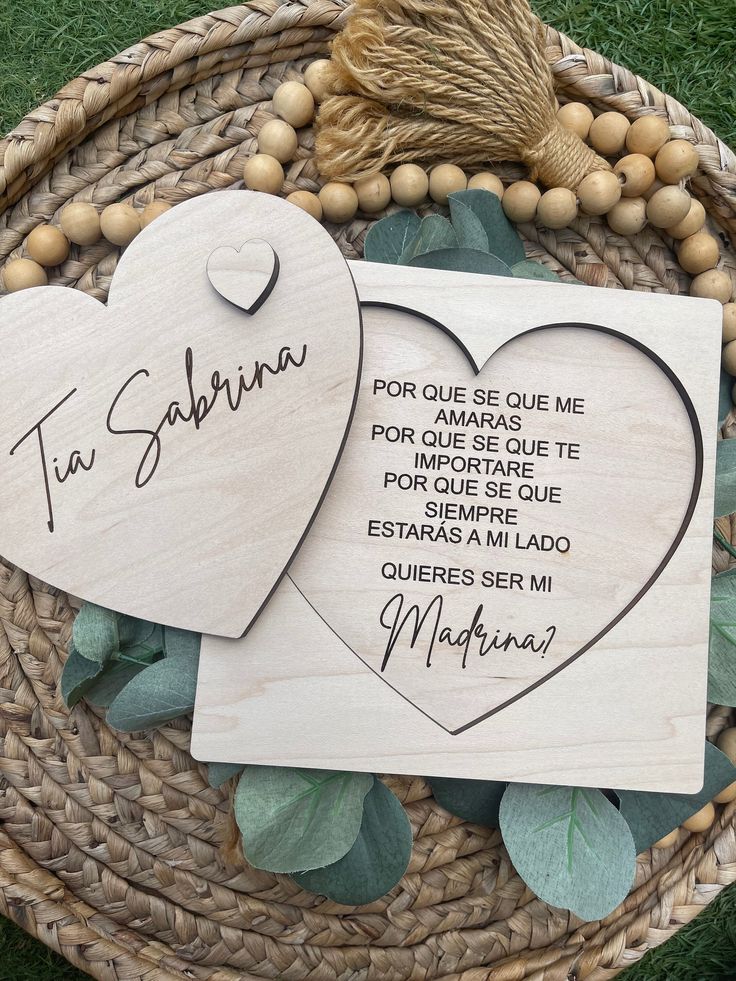 two wooden hearts with names on them sitting next to some green leaves and wood beads