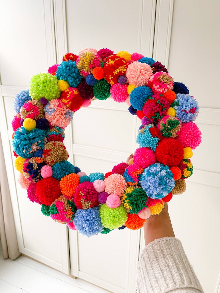 a person holding up a colorful wreath with pom - poms