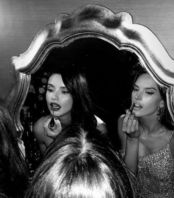 black and white photograph of two women brushing their teeth in front of a large mirror