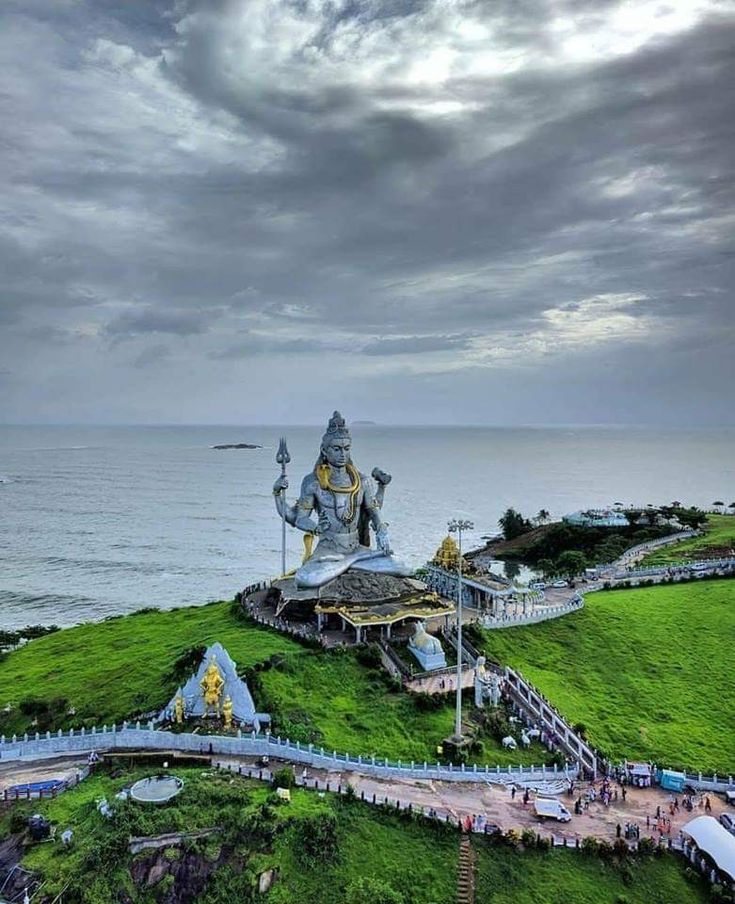 a large statue on top of a lush green hill next to the ocean