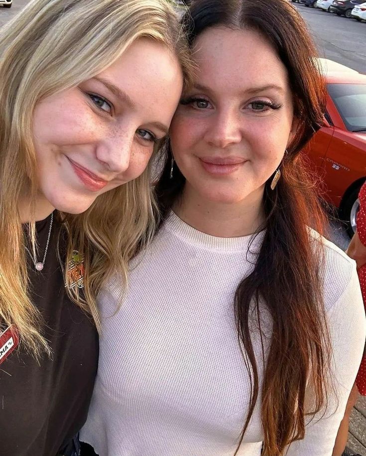 two young women standing next to each other in front of a parking lot full of parked cars