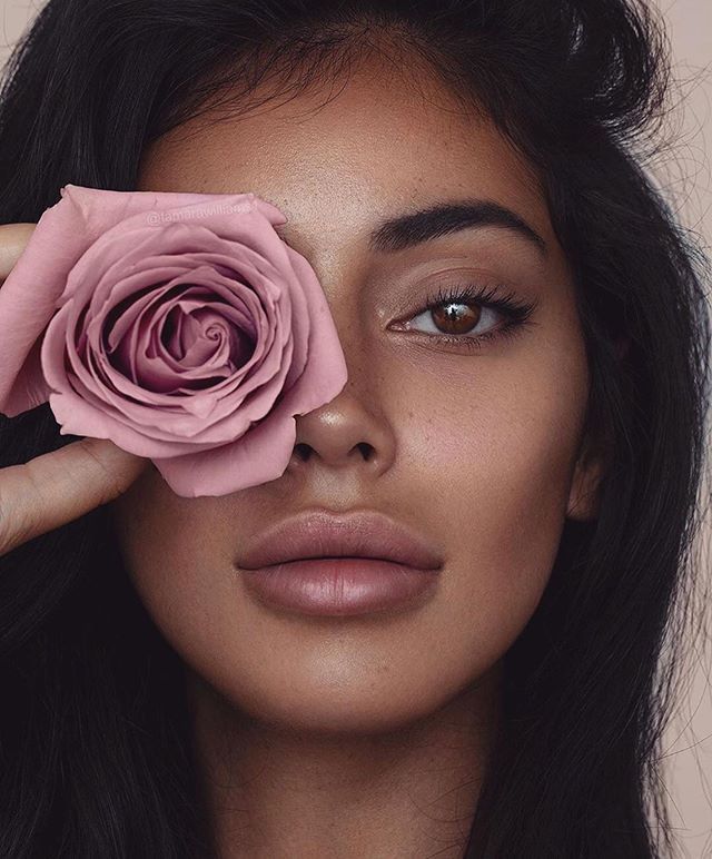 a woman holding a pink rose up to her eye