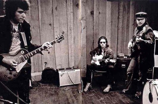 two men are playing guitars while another man is sitting on the floor in front of them