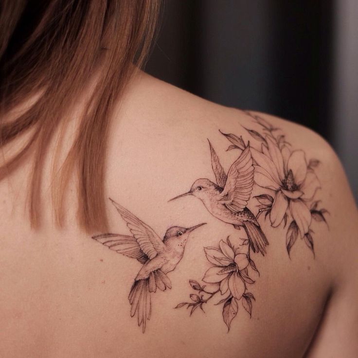 the back of a woman's shoulder with hummingbirds and flowers tattoo on it