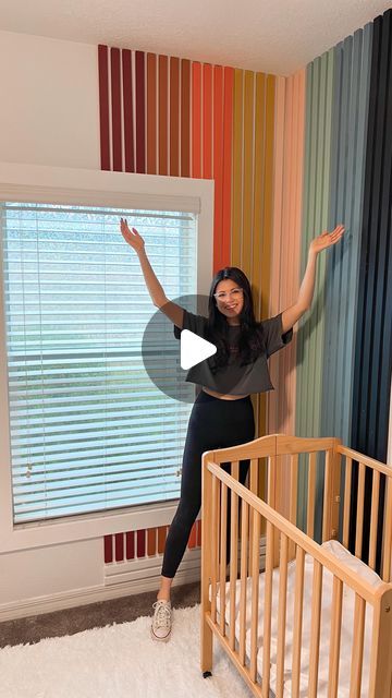 a woman standing next to a baby crib in front of a window with blinds