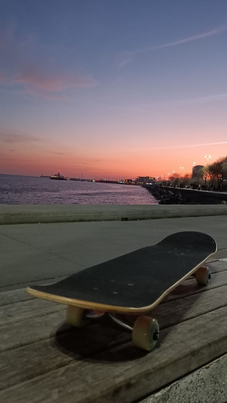 a skateboard sitting on top of a wooden bench near the ocean at sunset or dawn