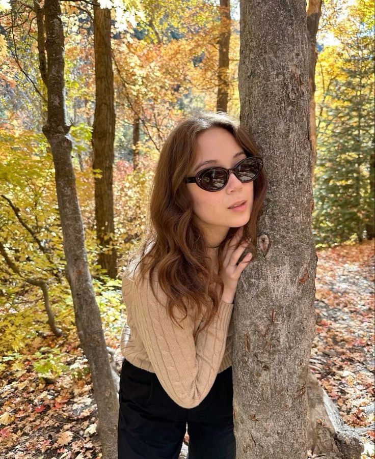 a woman wearing sunglasses leaning against a tree