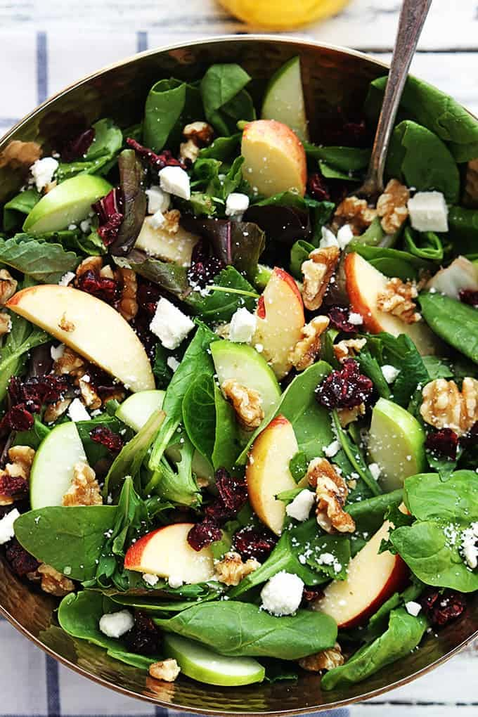 a salad with spinach, apples, walnuts and cranberries in a bowl