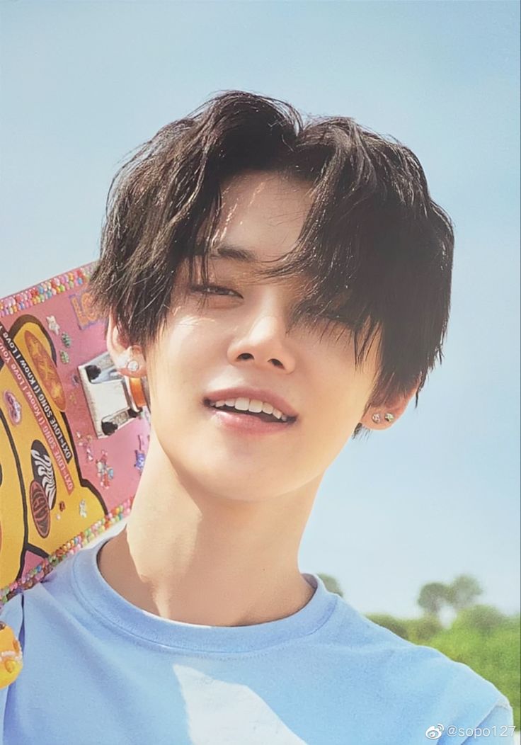 a young man holding a skateboard over his head and looking at the camera while wearing a blue t - shirt