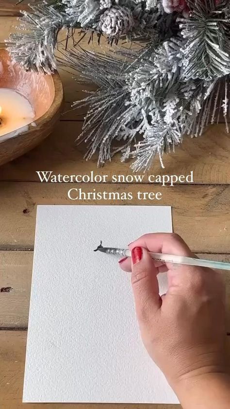 someone is holding a pen and writing on a piece of paper with watercolor snow capped christmas trees in the background