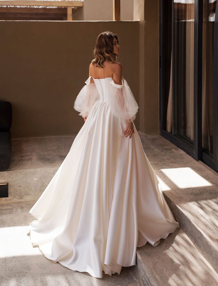 a woman in a white wedding dress is standing on the steps looking at something outside