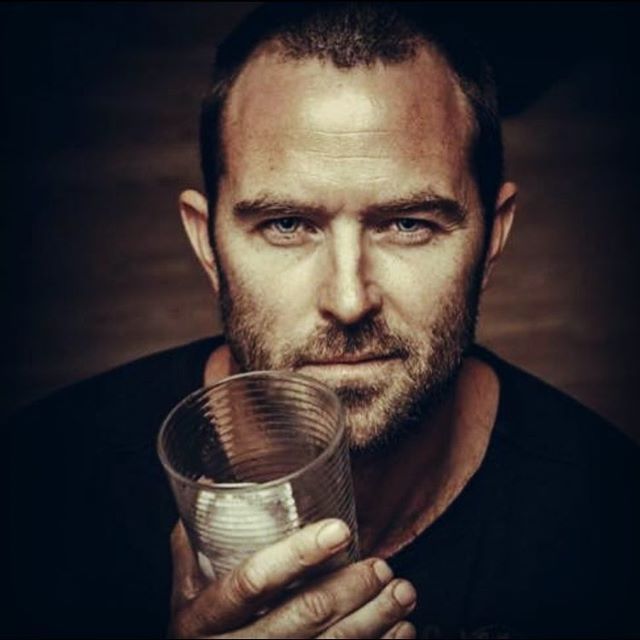 a man is holding a glass in his hand and looking at the camera with an intense look on his face