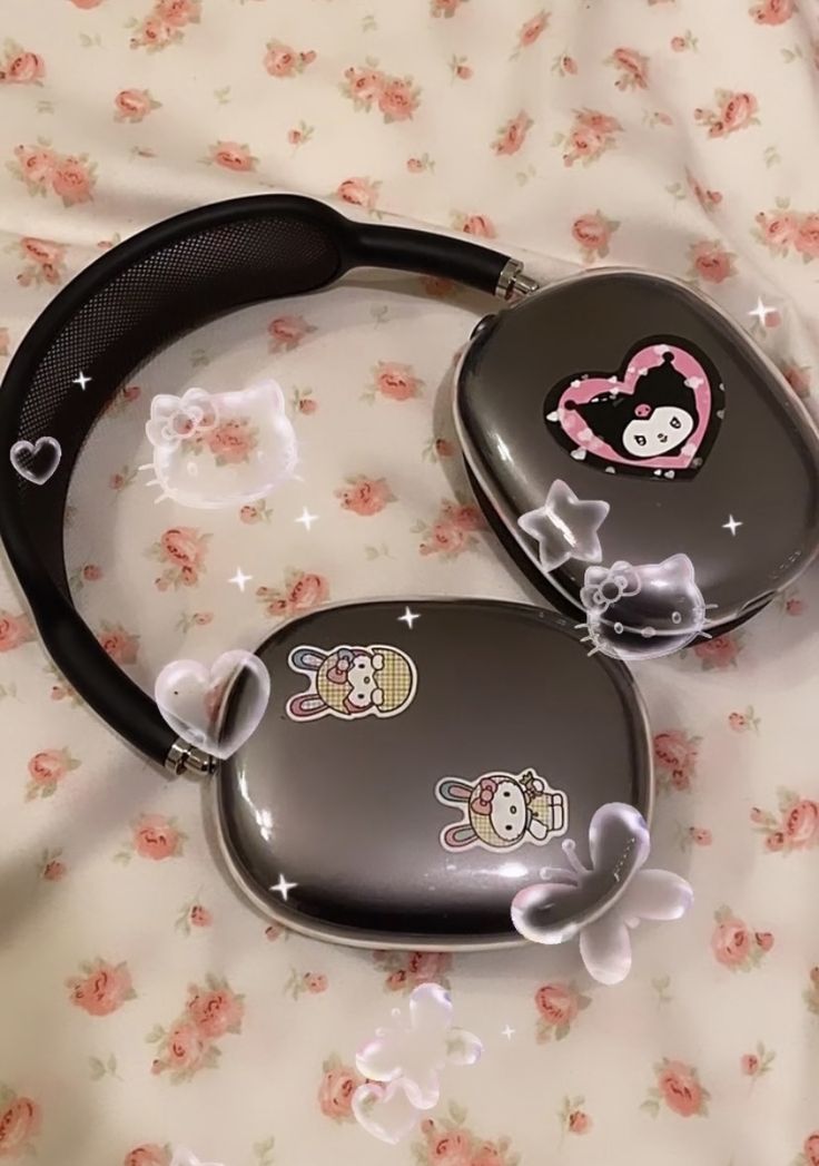 two black hello kitty ear buds laying on top of a flowery bed sheet with pink flowers