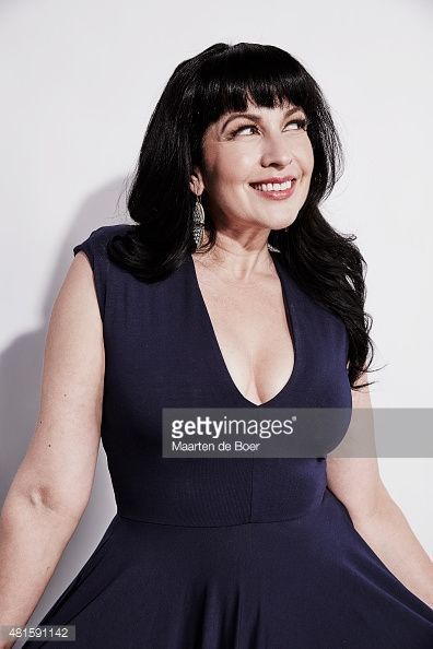 a smiling woman in a blue dress poses for a photo with her hands on her hips