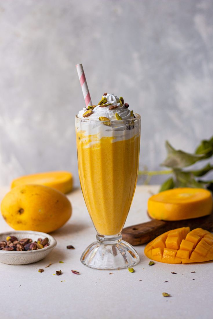 mango milkshake in a glass with whipped cream on top and fresh fruit around it