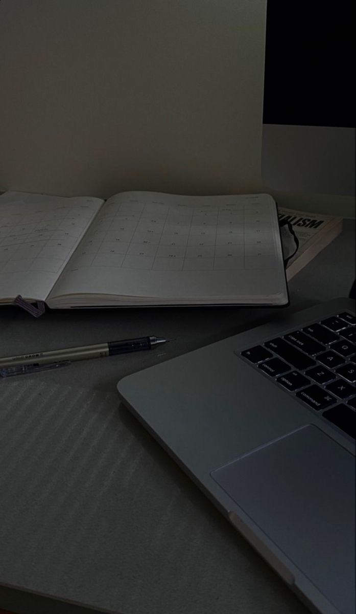 an open book sitting on top of a desk next to a laptop computer and pen