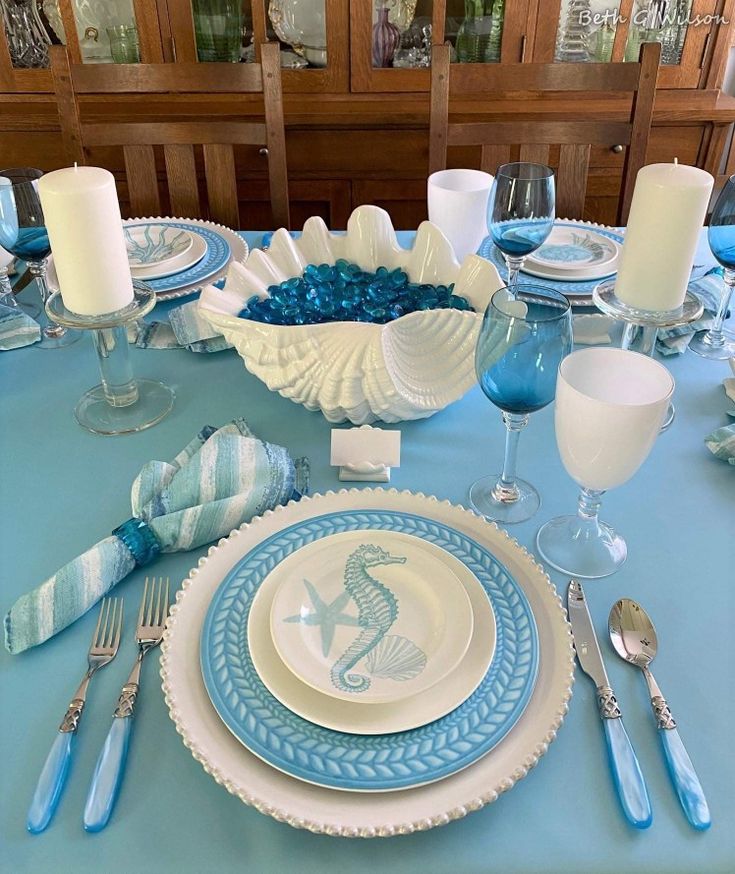 an ocean table set for summer with blue and white plates, napkins, silverware and candles