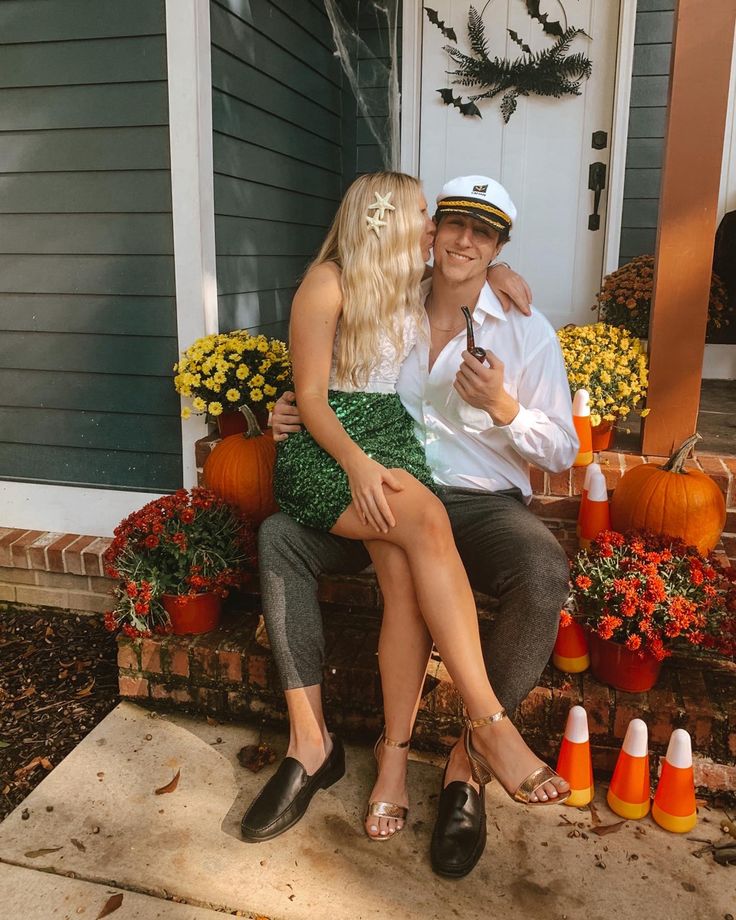 a man and woman are sitting on the steps in front of a house with pumpkins