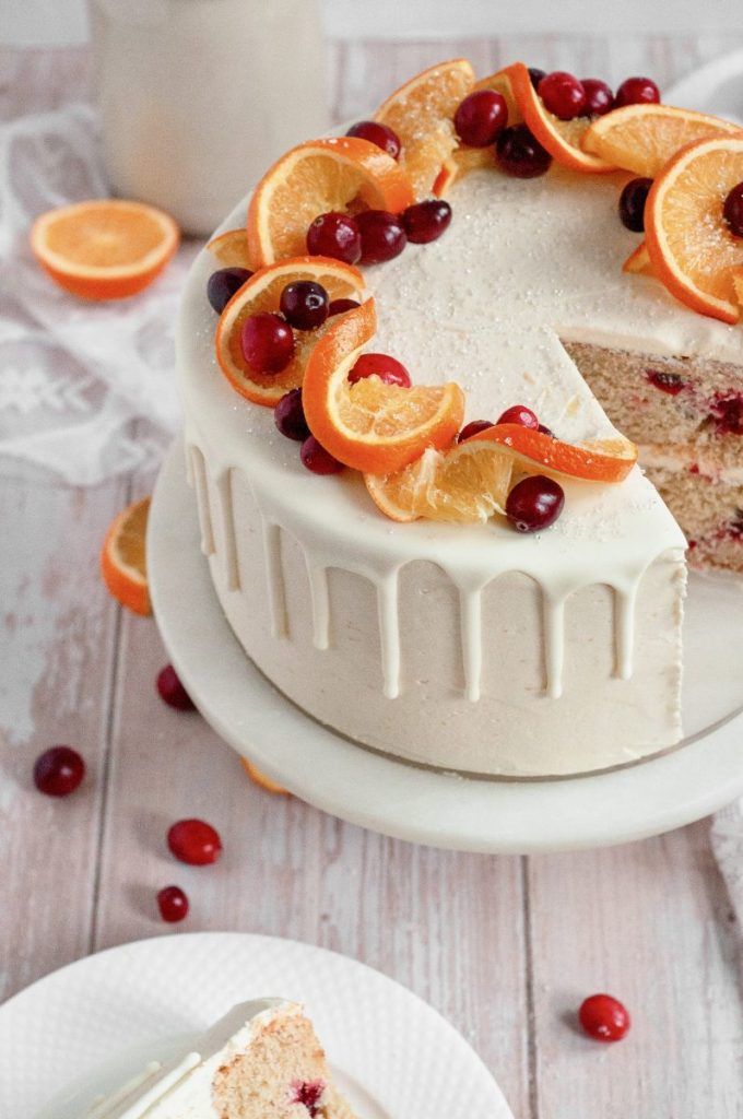 a white cake with oranges and cranberries on it sitting on a plate