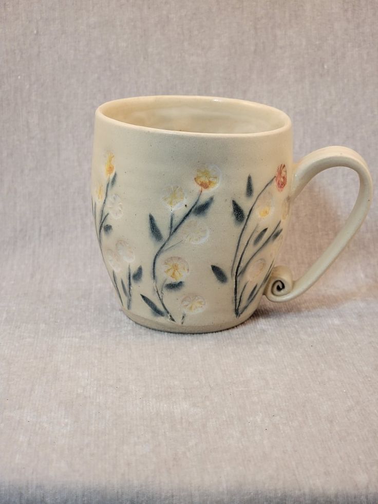 a white coffee cup with flowers painted on the outside and inside, sitting on a light colored surface