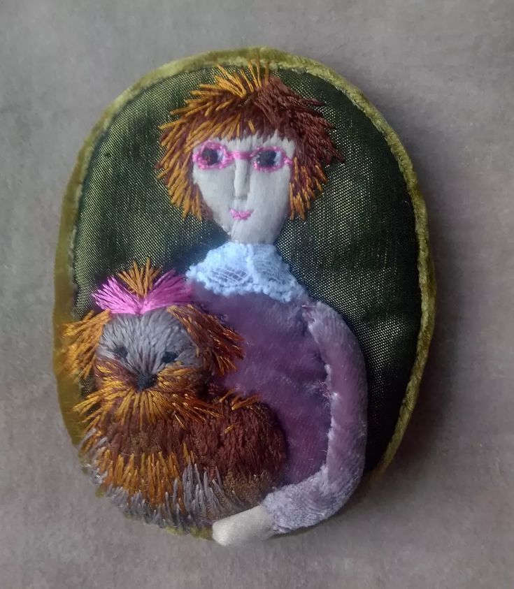 an embroidered doll holding a stuffed animal in it's lap