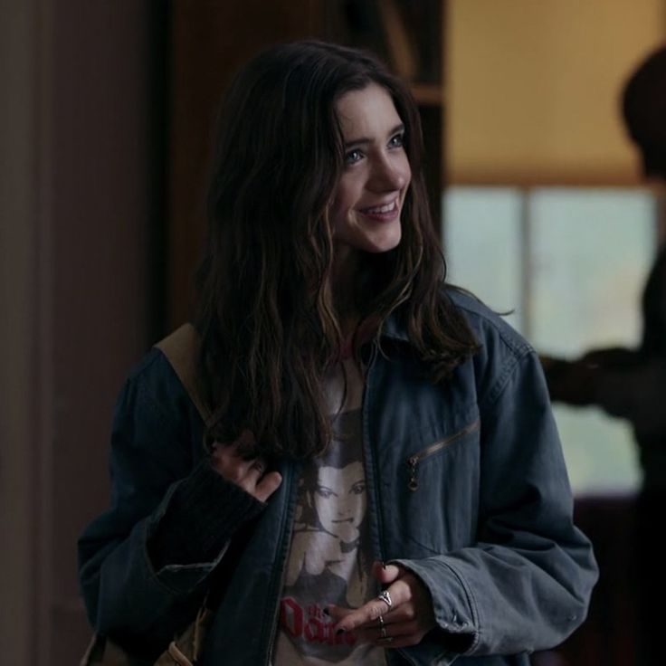 a woman with long hair wearing a denim jacket and smiling at someone in the background