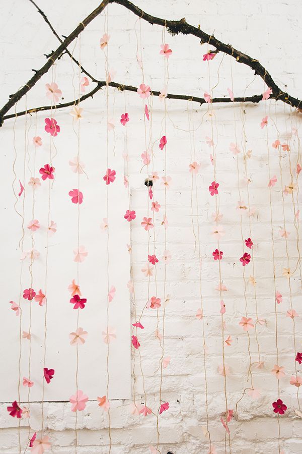 a white wall with pink and red flowers hanging from it's sides next to a tree branch