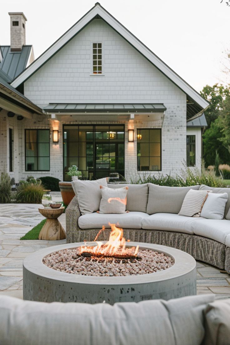 a fire pit sitting in the middle of a patio next to a white house with lots of windows