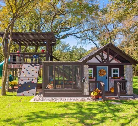 a backyard with a play house and climbing wall in the back yard, surrounded by trees