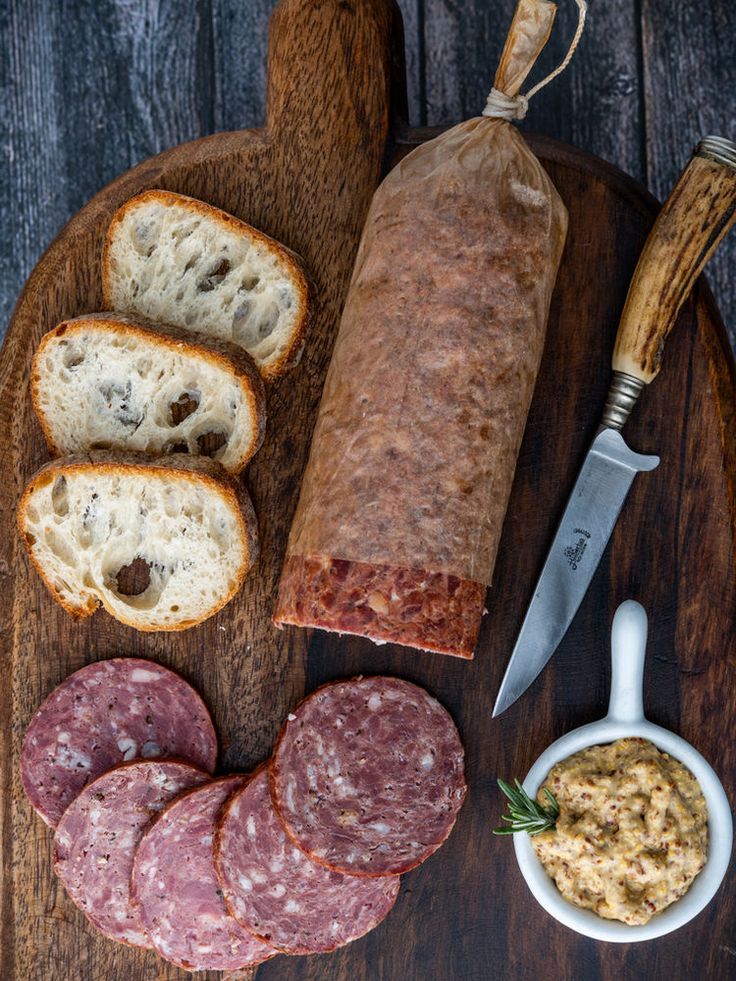 sausages and bread on a cutting board with a knife next to it, along with other ingredients