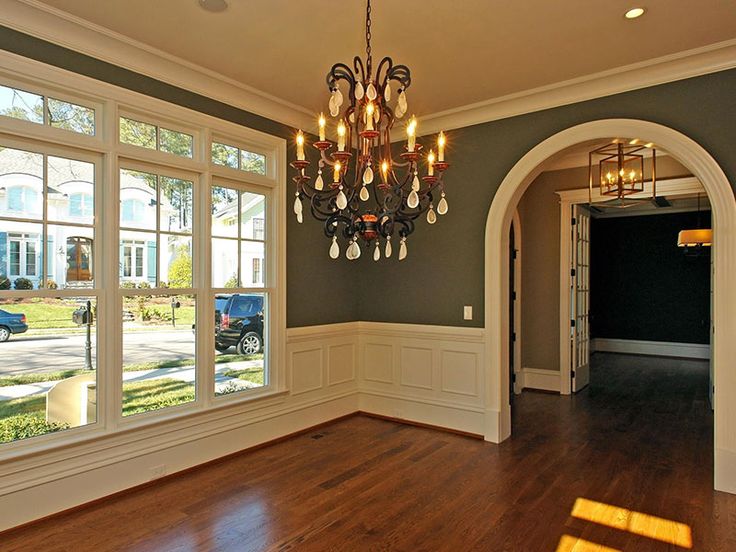 an empty living room with wood floors and chandelier hanging from the ceiling in front of large windows