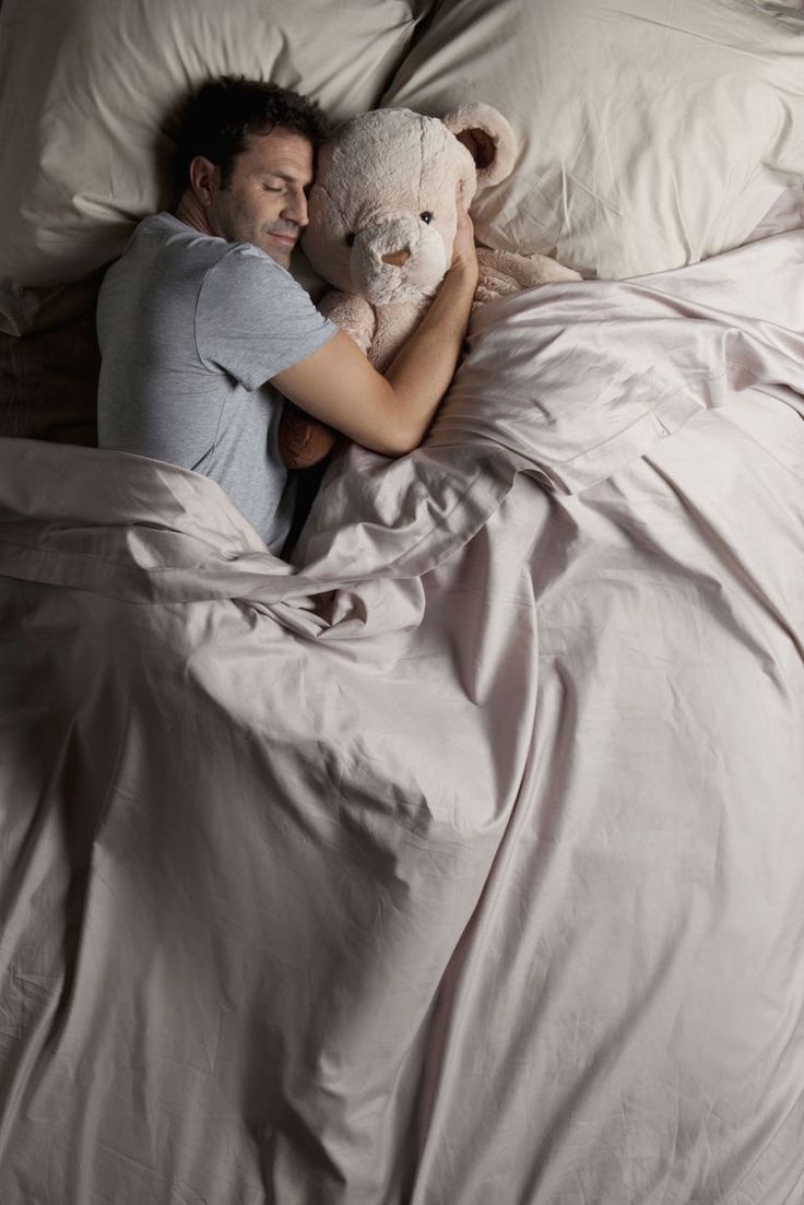 a man laying in bed holding a teddy bear