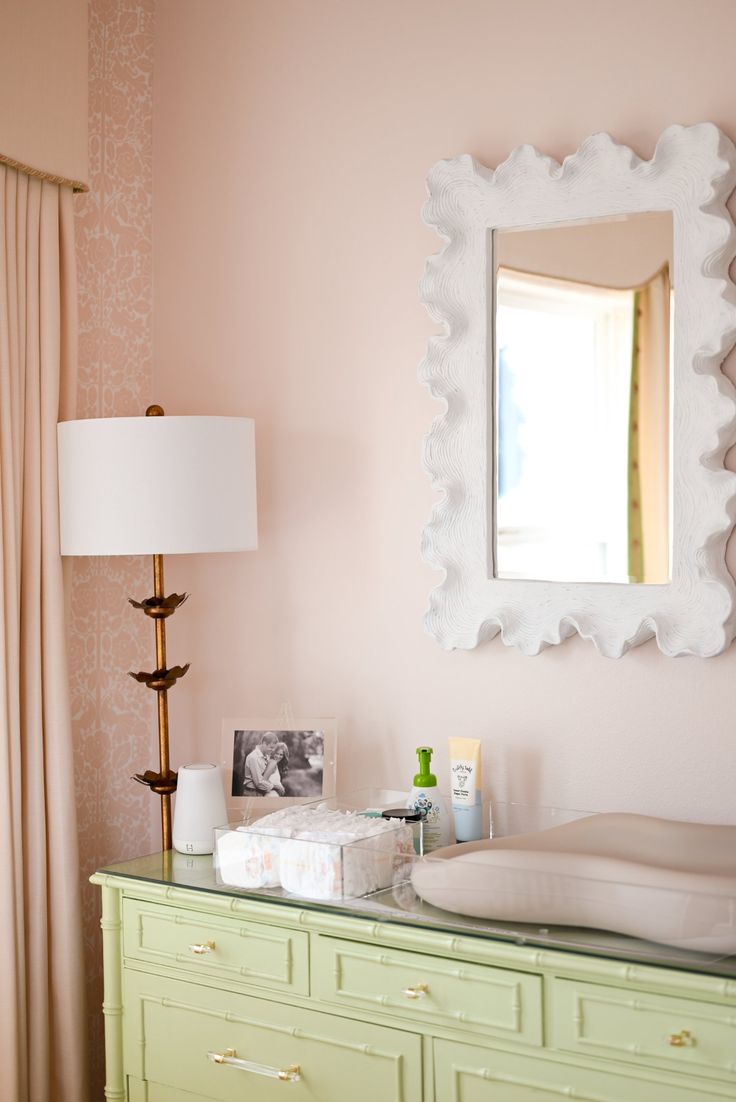 a dresser with a mirror, lamp and other items on it in a pink room