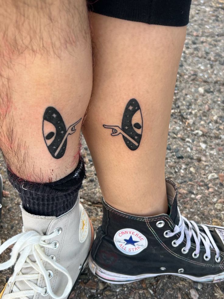 two people with tattoos on their legs and one has a pair of scissors in the middle